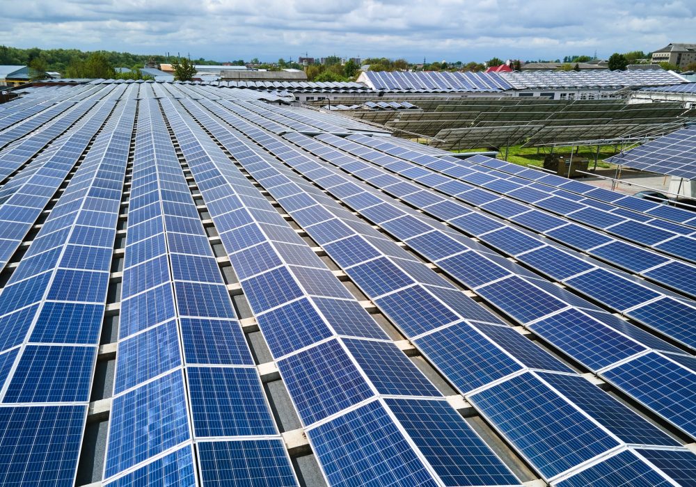 Aerial view of solar power plant with blue photovoltaic panels mounted on industrial building roof for producing green ecological electricity. Production of sustainable energy concept.